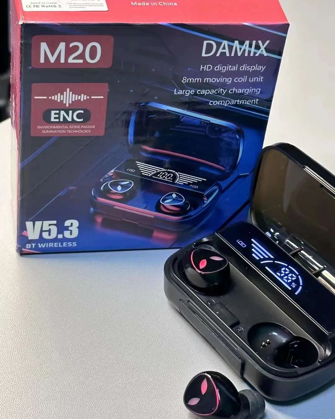Wireless earbuds with charging case and DAMIX M20 packaging on a light surface.