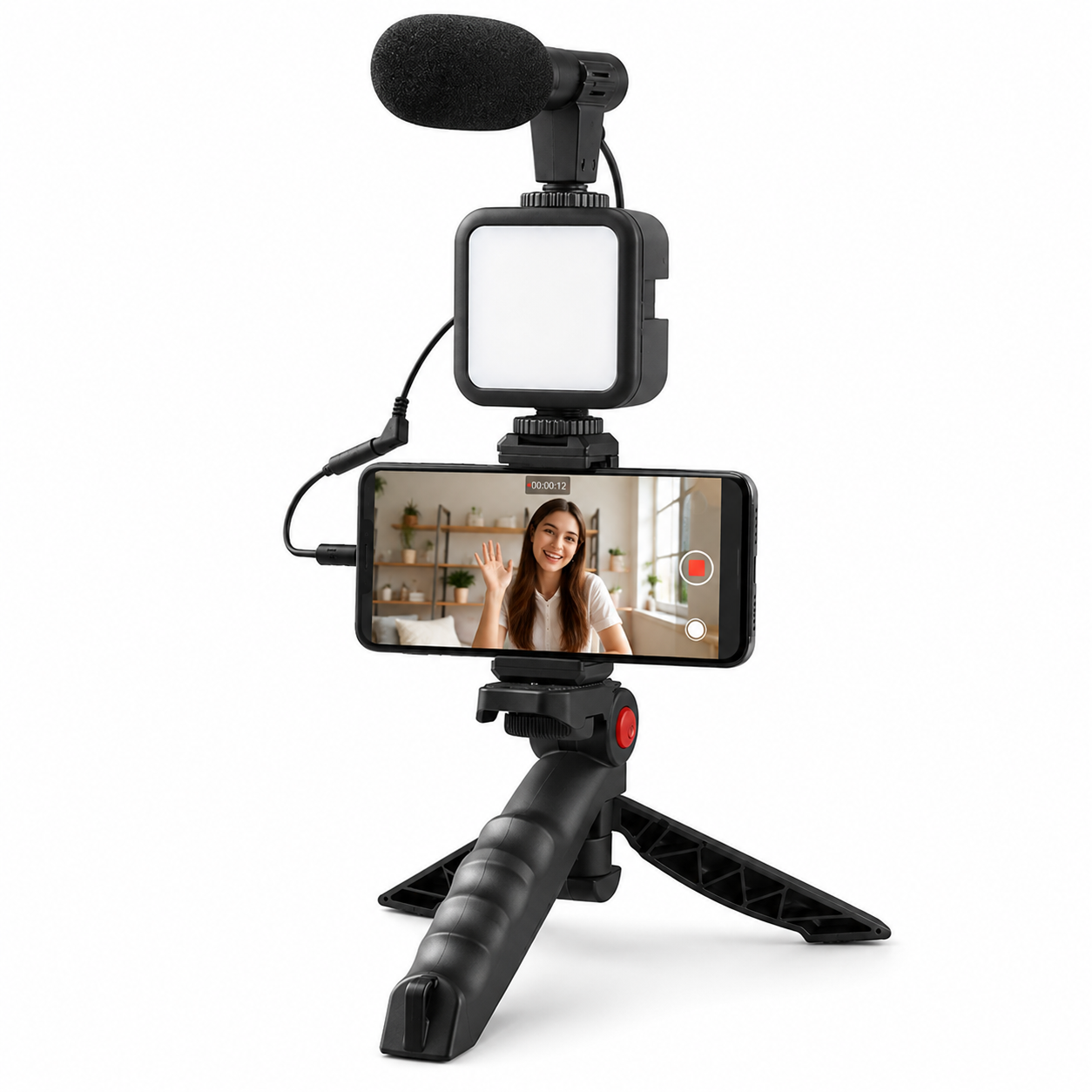 A black video recording setup on a small tripod, featuring a smartphone mounted in the center, a square light panel, and a shotgun-style microphone on top. The smartphone screen shows a video call interface with a woman waving.